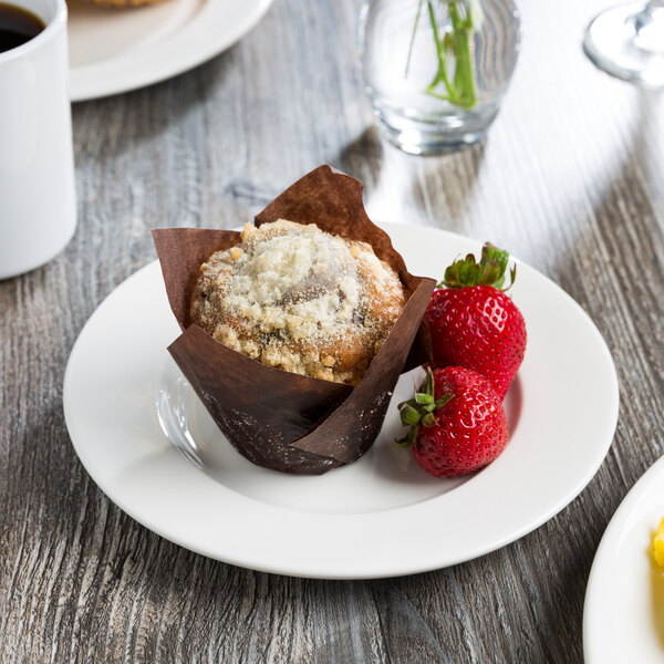 A Libbey white porcelain plate with a muffin and strawberries on it on a table next to coffee.