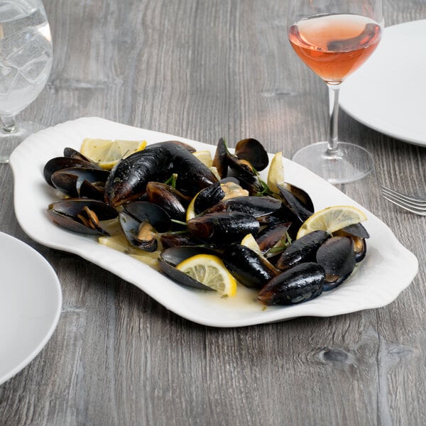 A Libbey Royal Rideau white porcelain handle platter with mussels and lemon wedges on a table.