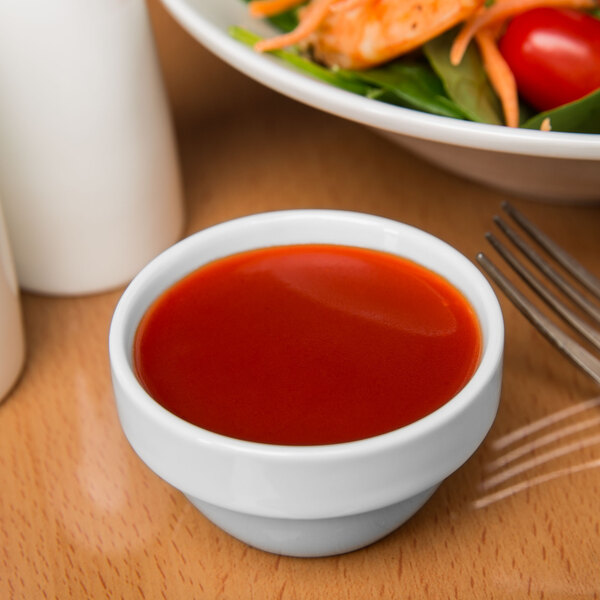 A white Libbey stacking ramekin filled with red sauce next to a plate of salad.