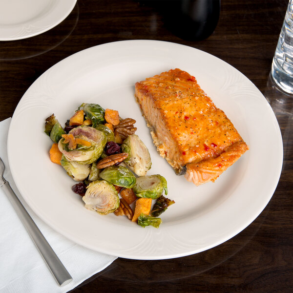 A piece of cooked salmon and vegetables on a white Reserve by Libbey Royal Rideau porcelain plate.