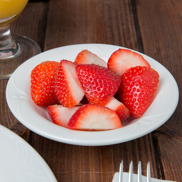 A bowl of strawberries on a table with a glass of orange juice.