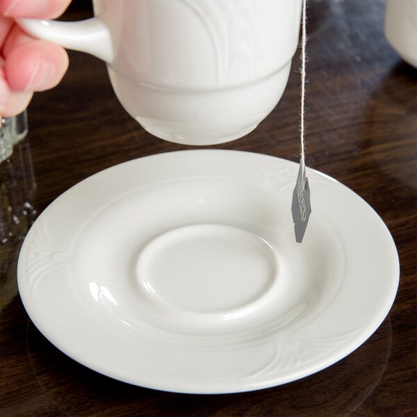A hand holding a tea bag over a white Royal Rideau tea saucer.