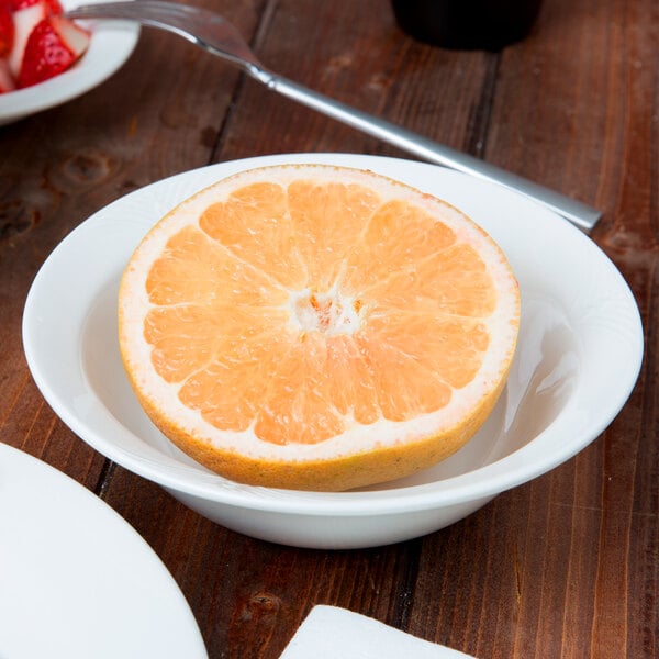 A bowl of grapefruit on a table with a half of an orange in it.