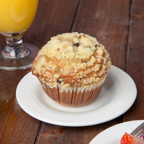 A muffin with crumbled topping on a Reserve by Libbey Royal Rideau white porcelain plate next to a glass of orange juice.
