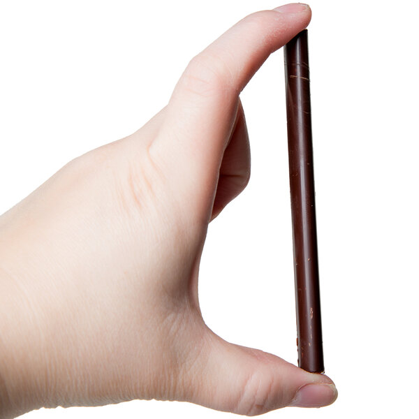 A hand holding a brown stick with chocolate decorations on it.