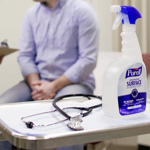 A man sitting at a table with a Purell Healthcare Surface Disinfectant spray bottle and a stethoscope.