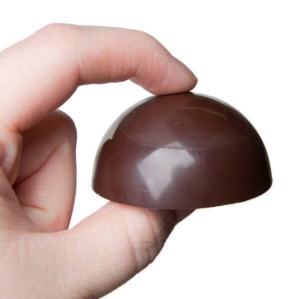 A hand holding a chocolate half sphere made with a Chocolate World candy mold.
