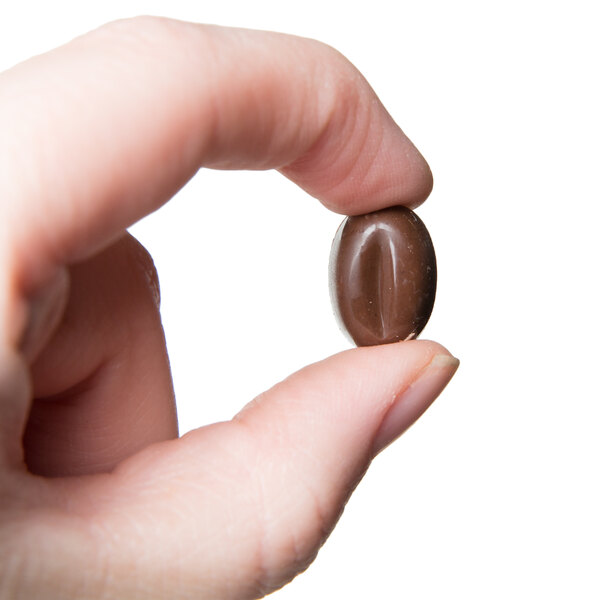 A hand holding a chocolate oval with coffee beans inside.