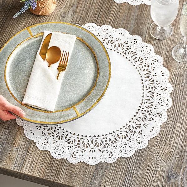 A hand holding a plate with a fork and knife on a Normandy lace doily.