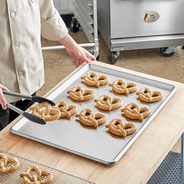 A person using a Baker's Mark stainless steel sheet pan to prepare pretzels.