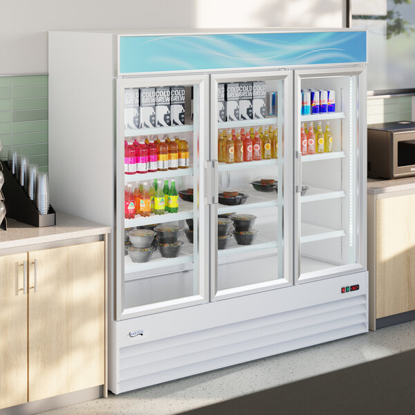 A large white glass door merchandiser refrigerator with three swing doors and LED lighting, stocked with beverages and food items.