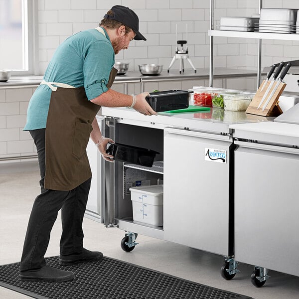 A man in an apron using an Avantco worktop freezer in a commercial kitchen.
