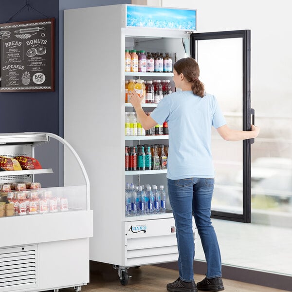 A woman standing in front of an Avantco white swing glass door refrigerator.