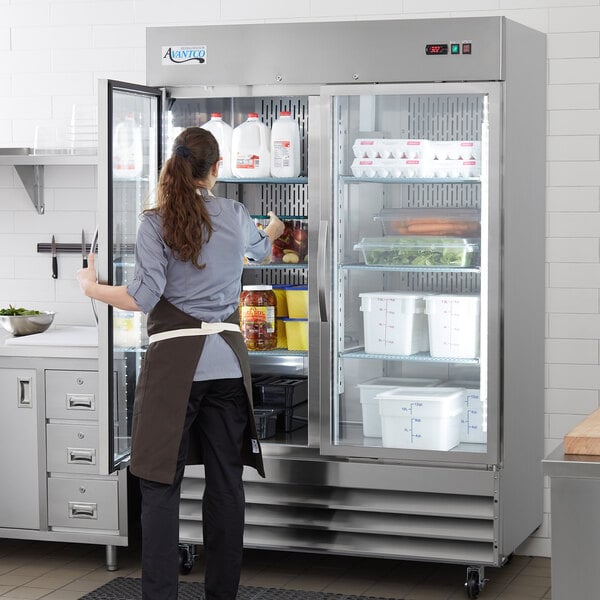 A woman standing in front of an Avantco stainless steel glass door reach-in refrigerator.