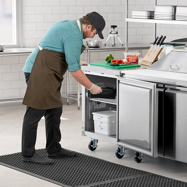 A man in a professional kitchen using an Avantco undercounter freezer.