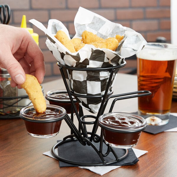 A person holding a fried food cone basket with ramekins of sauce.