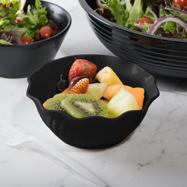 A bowl of fruit in a Cambro black swirl bowl on a table with other bowls.