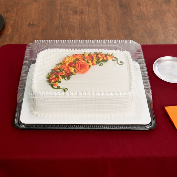 A white sheet cake with orange flowers in a D&W Fine Pack plastic container with a clear lid.