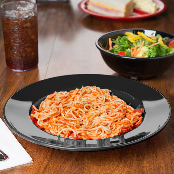 A bowl of salad with vegetables and a plate of spaghetti with sauce on a table.