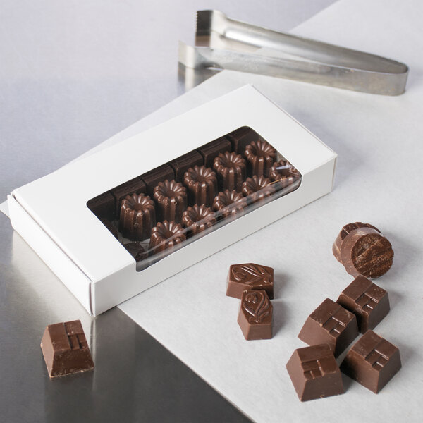 A white rectangular candy box with a window filled with chocolates on a table.