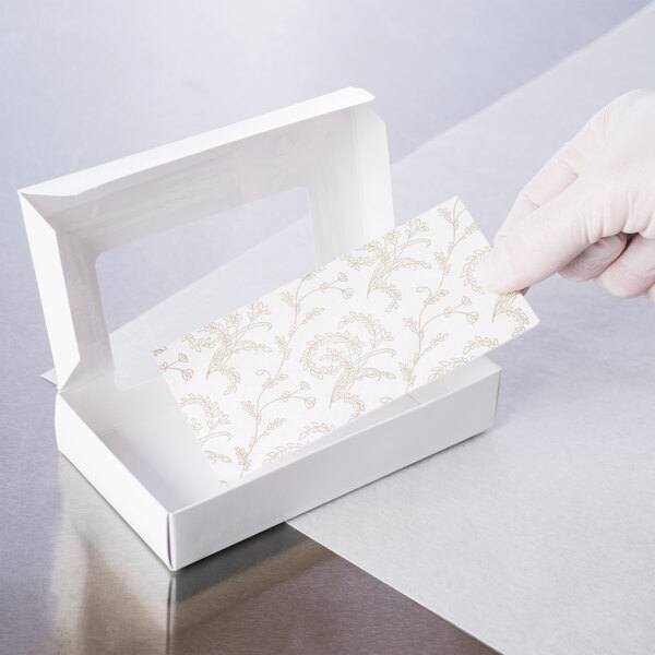 A gloved hand holding a white Candy Box Pad with a gold floral pattern inside.