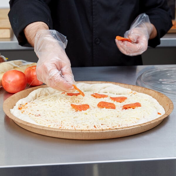 A person wearing plastic gloves putting cheese on a pizza.
