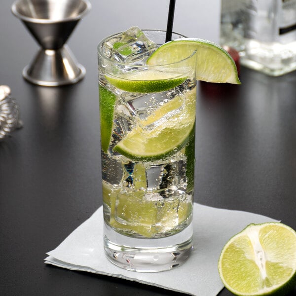 A Reserve by Libbey beverage glass with liquid, ice, and lime slices with a straw.