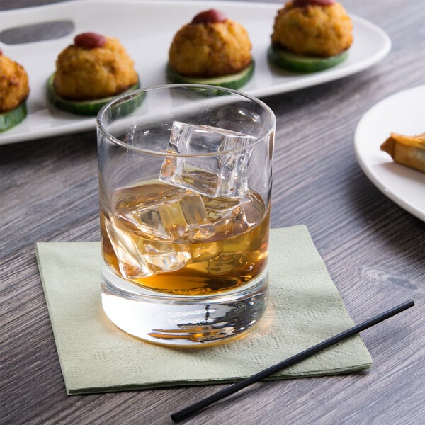 A Reserve by Libbey Modernist rocks glass filled with whiskey and ice on a table with a plate of food.
