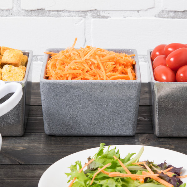 A table with a row of Tablecraft Contemporary Collection granite bowls filled with shredded carrots.