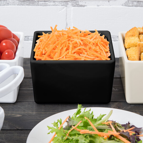 A black Tablecraft bowl filled with shredded carrots on a table.