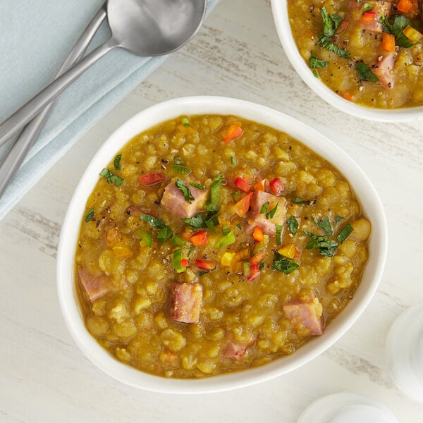 A bowl of split pea soup with ham and vegetables.