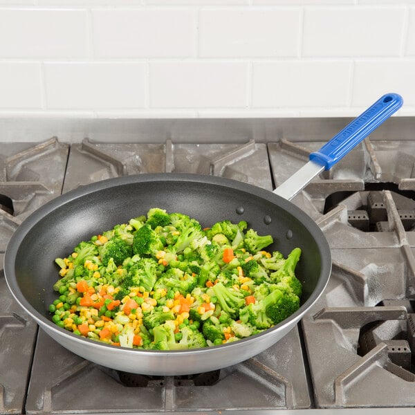 A Vollrath Wear-Ever aluminum non-stick fry pan with broccoli and corn cooking inside, with a blue Cool Handle.