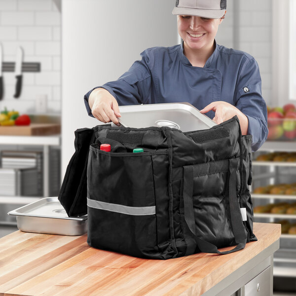 A woman in a kitchen opening a black ServIt food delivery bag.