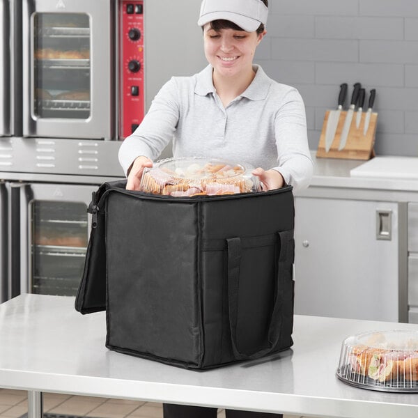 A woman holding a black Choice insulated food delivery bag full of food.