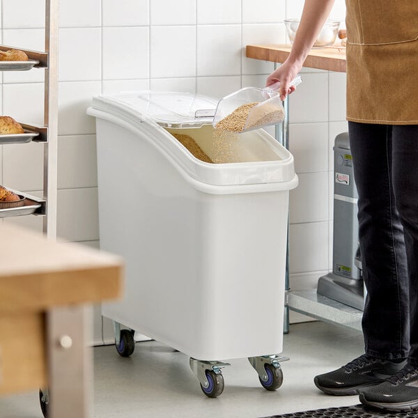 A white slant top mobile ingredient storage bin with a sliding lid and scoop, designed for bulk storage in kitchens or bakeries.