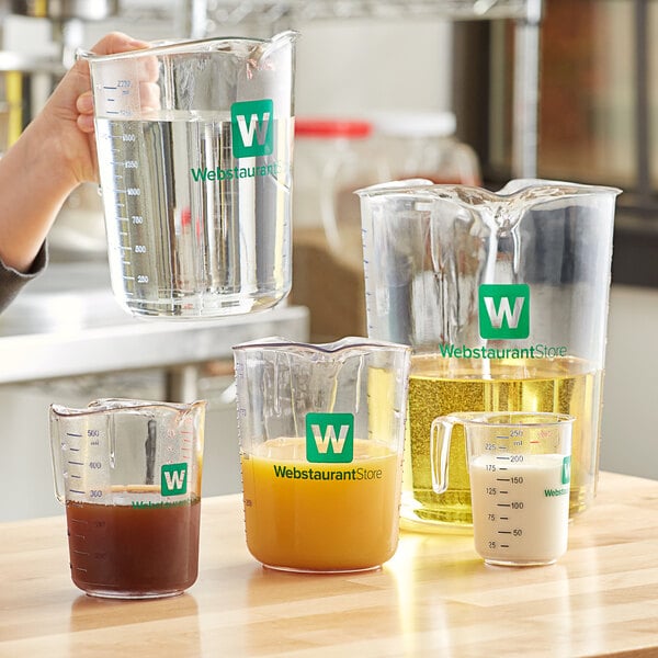 A hand pours clear liquid into a WebstaurantStore clear polycarbonate measuring cup on a counter.