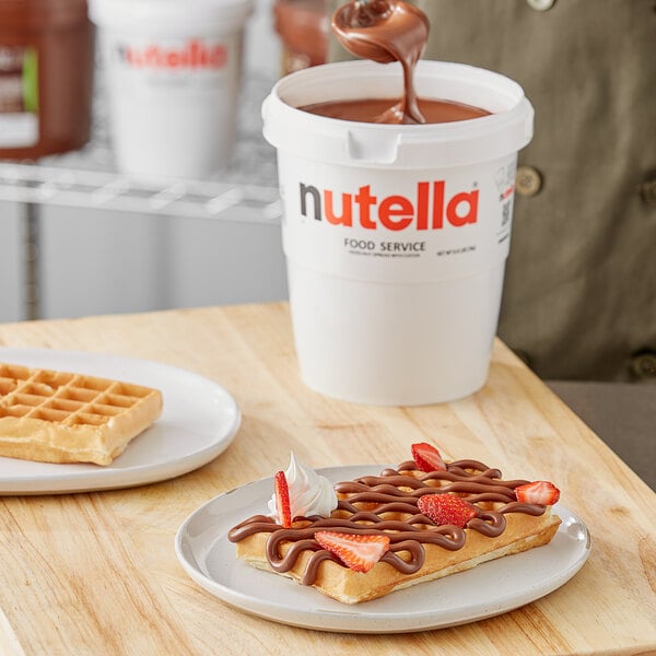 A waffle with strawberries and Nutella spread on a wooden board.