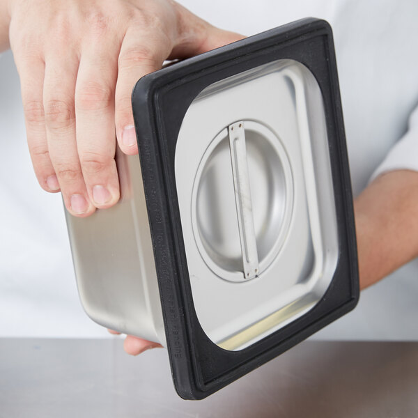 A hand using a Vollrath black silicone band to hold a metal container over a counter.