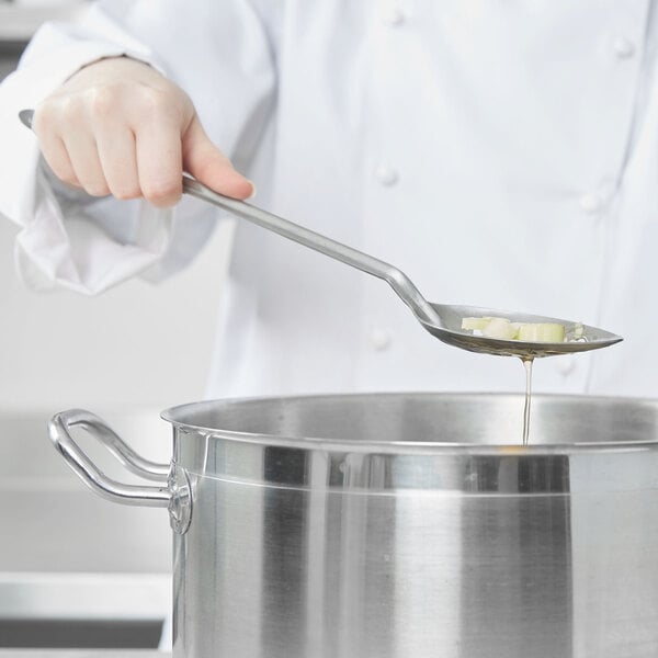 A person using a Vollrath slotted stainless steel basting spoon to stir food in a pot.