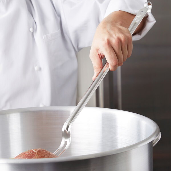 A hand using a Vollrath hooked handle pot fork to stir meat in a large pot.