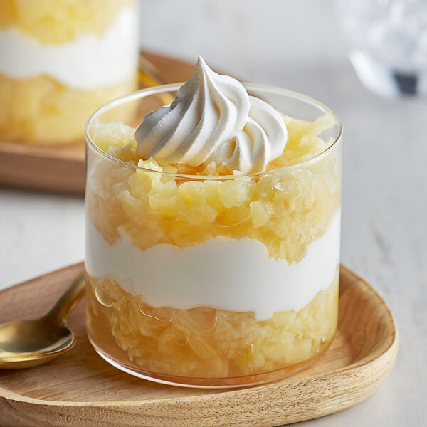 A glass of dessert with whipped cream and pineapple with a spoon.