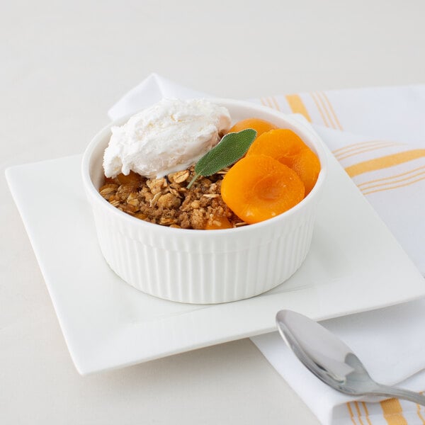 A white bowl of apricot halves in light syrup on a white plate with a spoon.
