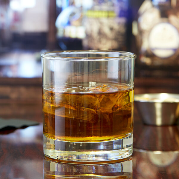 A Libbey old fashioned glass filled with amber liquid and ice on a table.