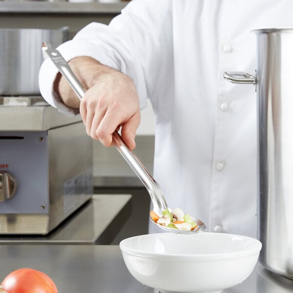A chef using a Vollrath hooked slotted spoon to stir food in a bowl.