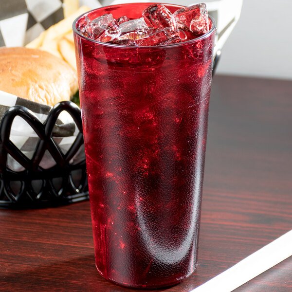 A Cambro ruby red plastic tumbler filled with ice and red liquid on a table with a burger.