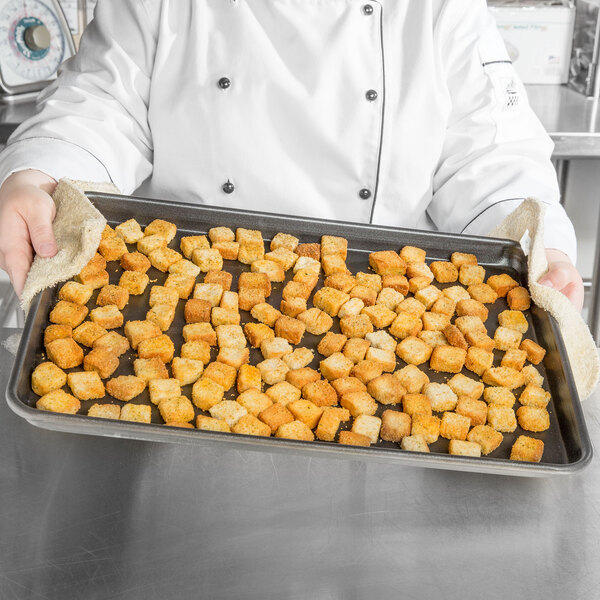 A person holding a Vollrath Wear-Ever bun pan full of croutons.