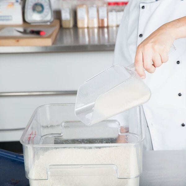 A person using a Baker's Mark clear plastic utility scoop to pour rice into a container.
