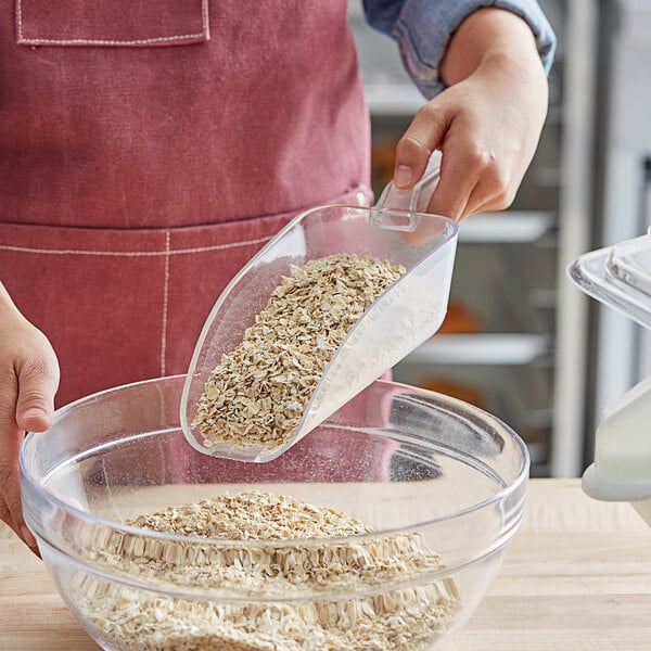 A person using a Choice clear plastic utility scoop to pour oats into a bowl.