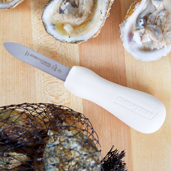 A Dexter-Russell white handled stainless steel oyster knife on a cutting board.