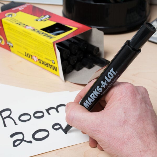 A hand using an Avery Marks-A-Lot black desk style marker to write on a piece of paper.